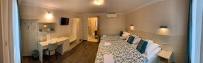 Quarto de hotel com escrivaninha, duas camas, televisão e banheiro.