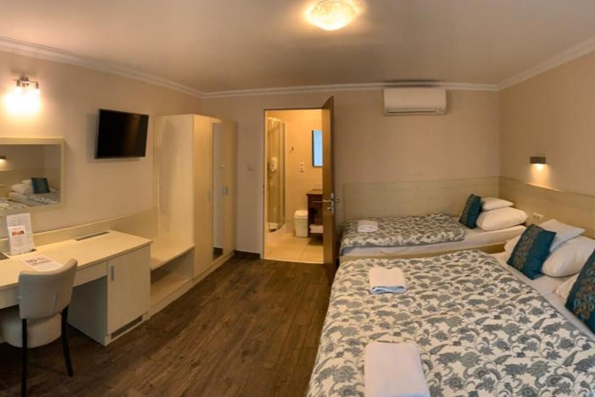 Quarto de hotel com escrivaninha, duas camas, televisão e banheiro.