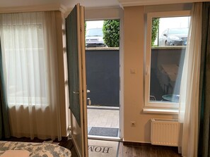 Habitación de hotel con cama, ventana con vista a coches estacionados y puerta que da a un espacio al aire libre.