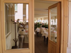 Un comedor interior con mesas y sillas, una entrada visible y un letrero que indica aire acondicionado.