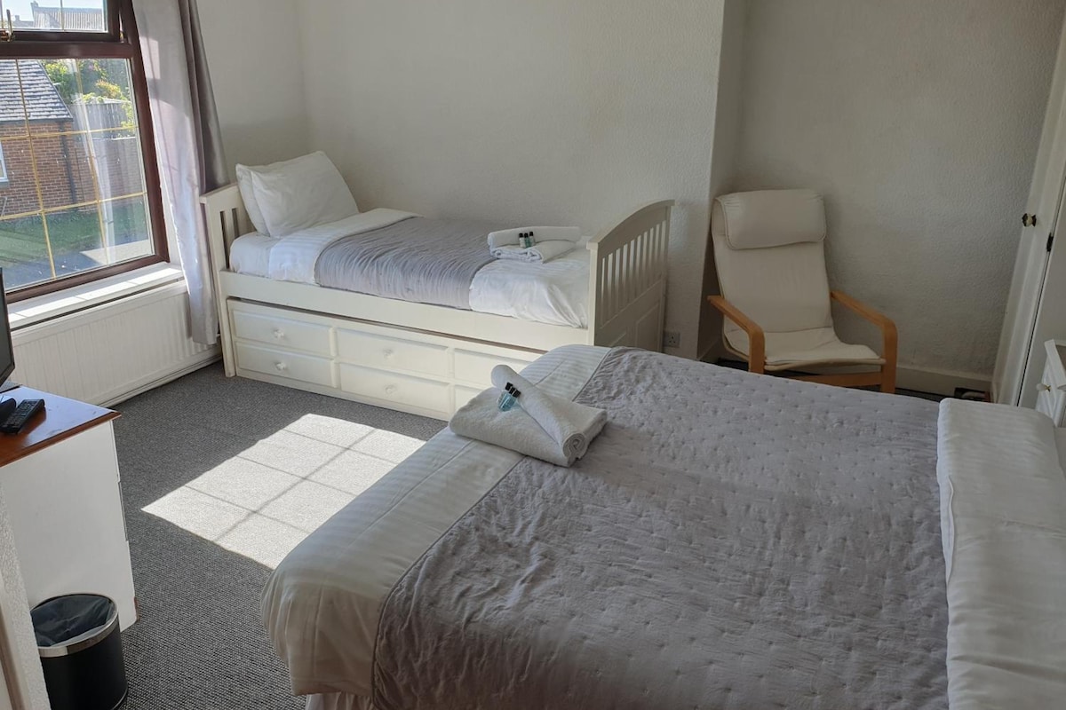 A hotel room with two beds, a chair, a desk, and a window.