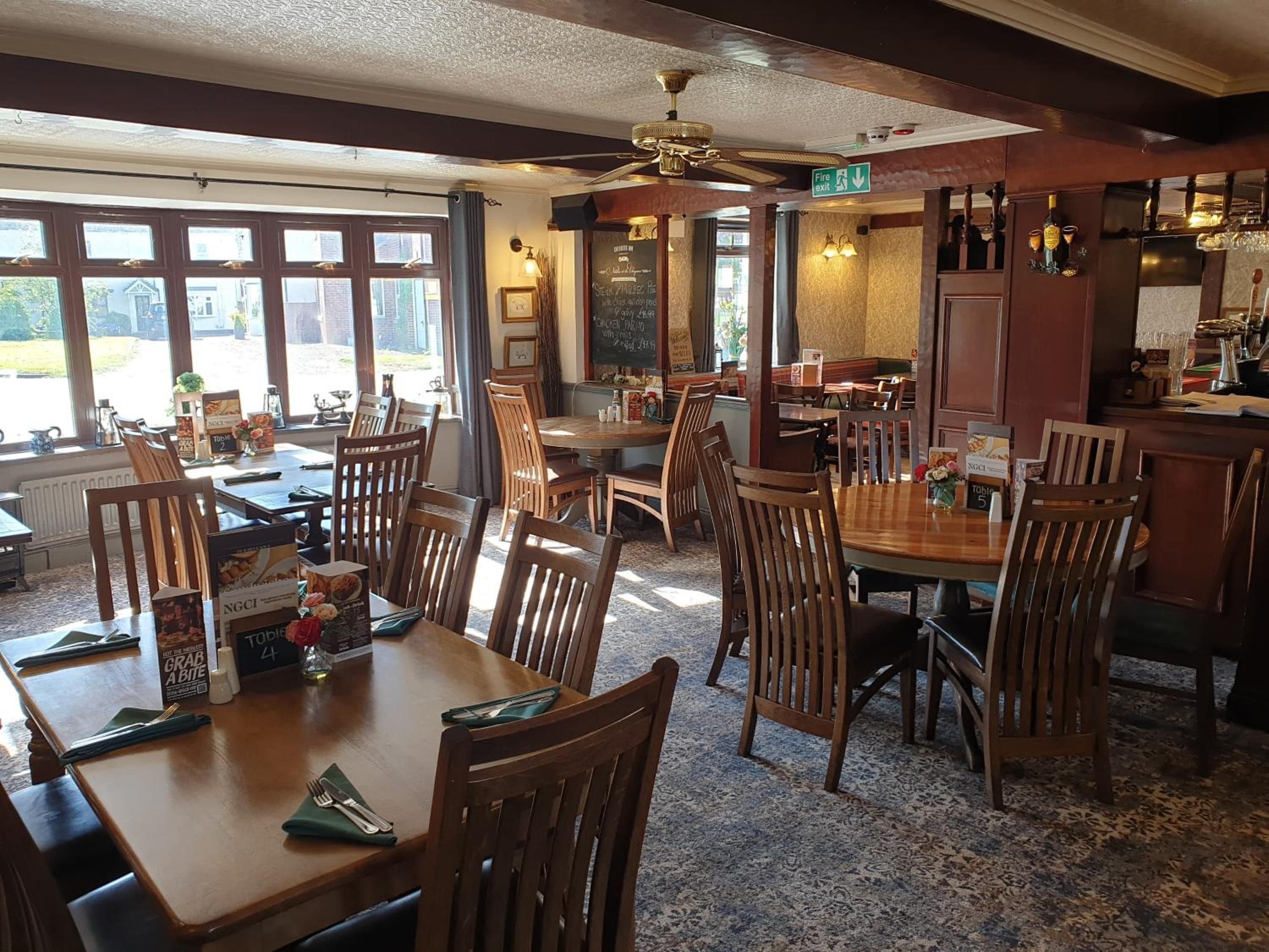 A restaurant interior with wooden tables and chairs, a bar area, and a view through large windows.