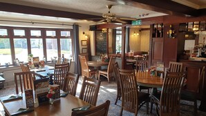 A restaurant interior with wooden tables and chairs, a bar area, and a view through large windows. - The Chequers Inn (Darlington)