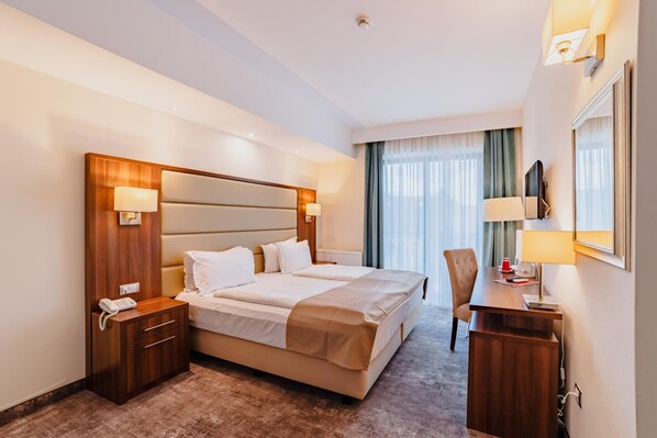 A hotel room with a large bed, bedside tables, a desk, a chair, and a window with curtains. - Radsor Hotel (Rasnov)