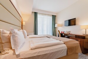 Habitación de hotel con cama, escritorio, silla, televisor y ventana con cortinas.
