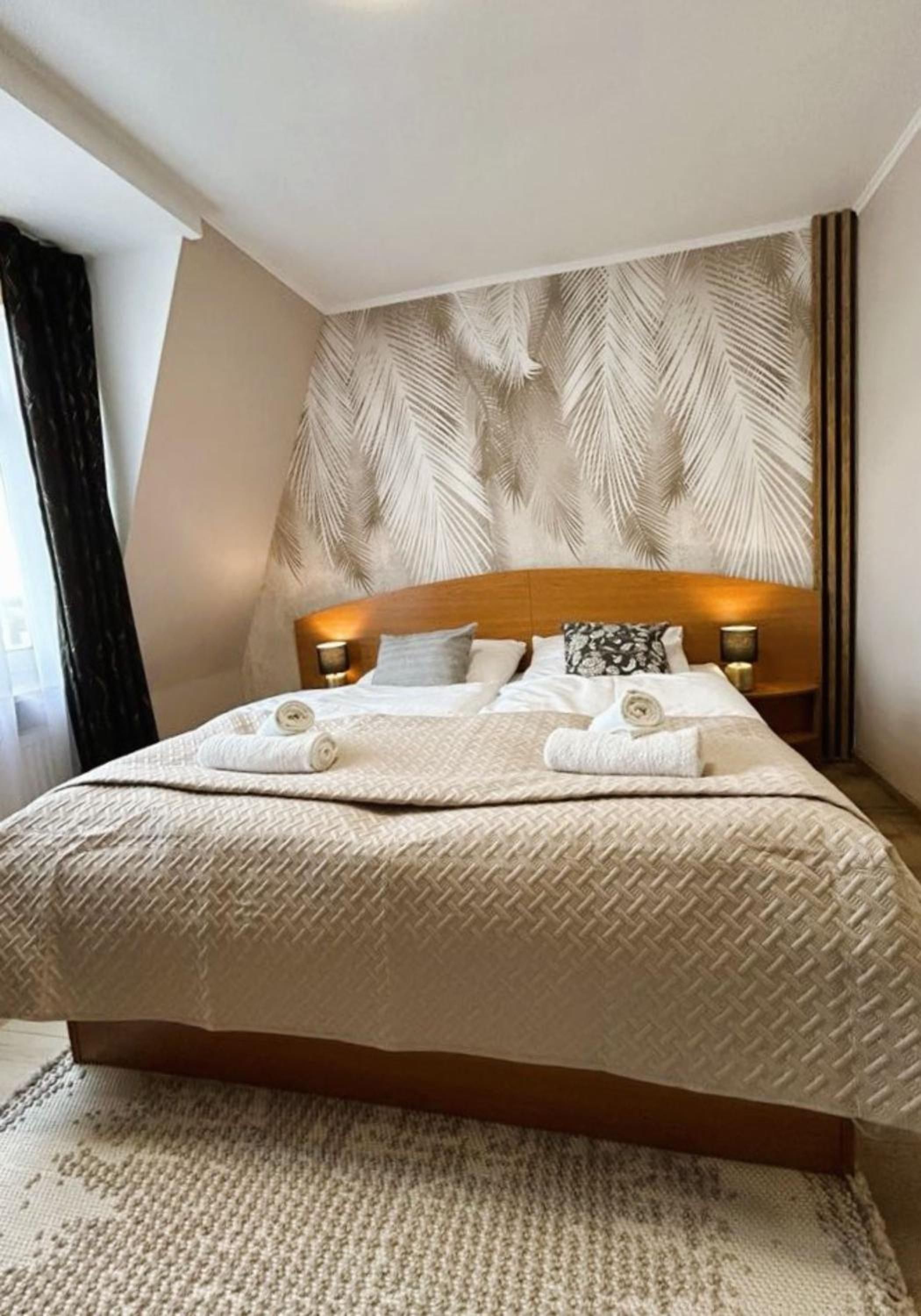 Ein Hotelzimmer mit einem großen Bett, einem Blattmuster-Kopfende, zwei Nachttischlampen und einem gemusterten Teppich.