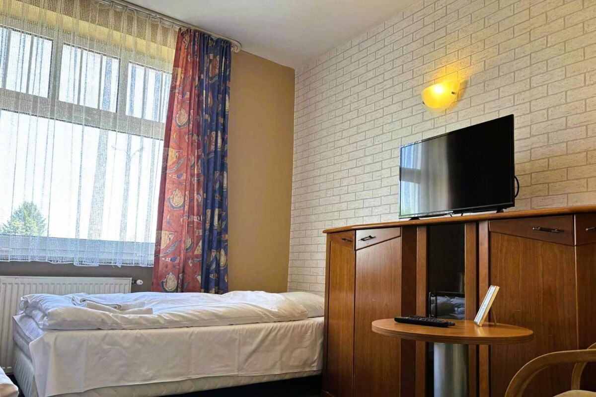 Habitación de hotel con cama, televisor sobre un mueble de madera, una mesita redonda y un sillón.