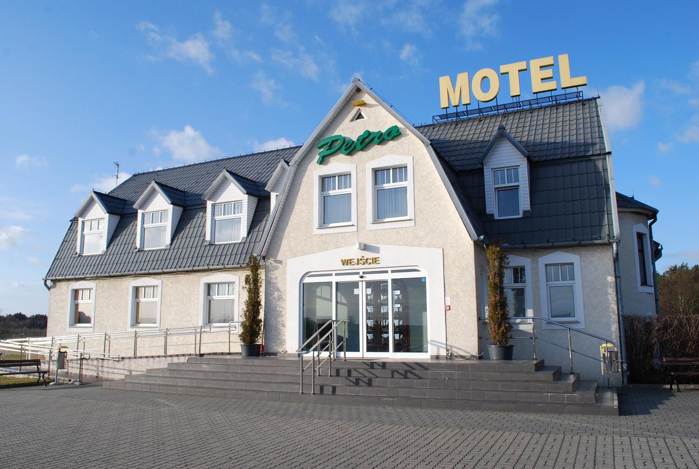 En toetages bygning med et 'Motel' skilt, et 'Petro' skilt og et 'Węcze' skilt.