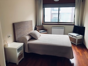 Ett välordnat hotellrum med en säng, en stol, ett TV-bord och ett fönster med gardiner.