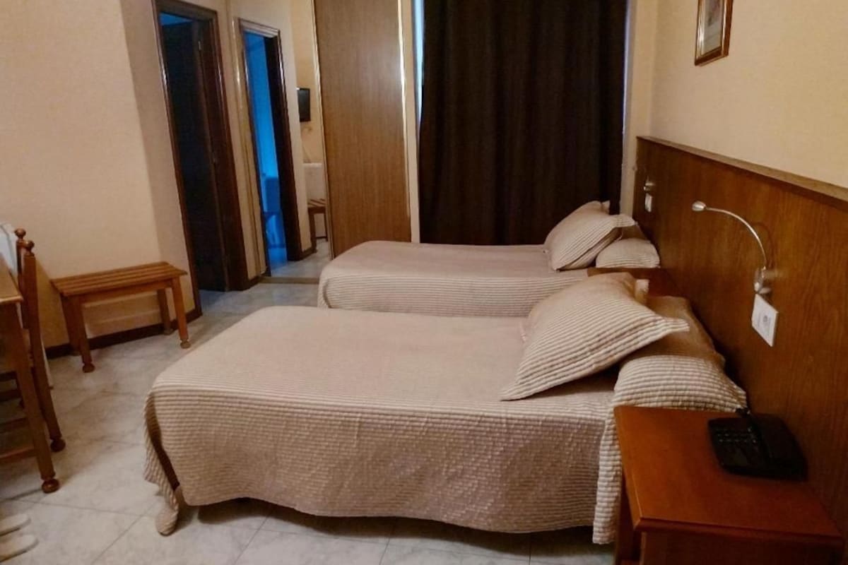 A hotel room with a bed, bedside table, and a lamp.