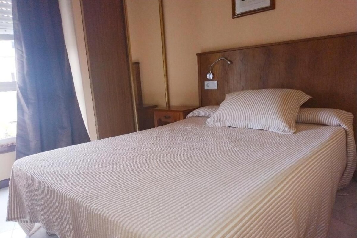 A neatly made bed with a striped bedspread, a wooden headboard, and a bedside table with a lamp.