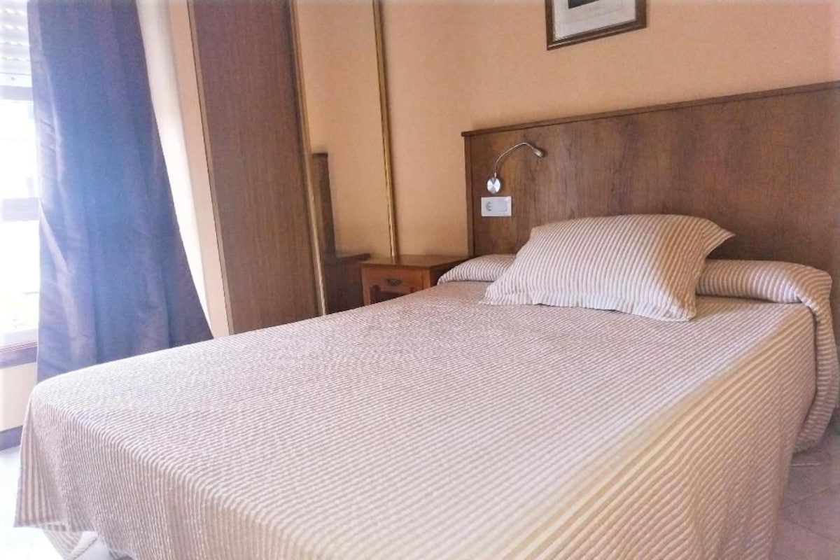 A neatly made bed with a striped bedspread, a wooden headboard, and a bedside table with a lamp.