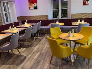 Interior de un restaurante con varias mesas y sillas, un suelo estampado y obras de arte en las paredes.