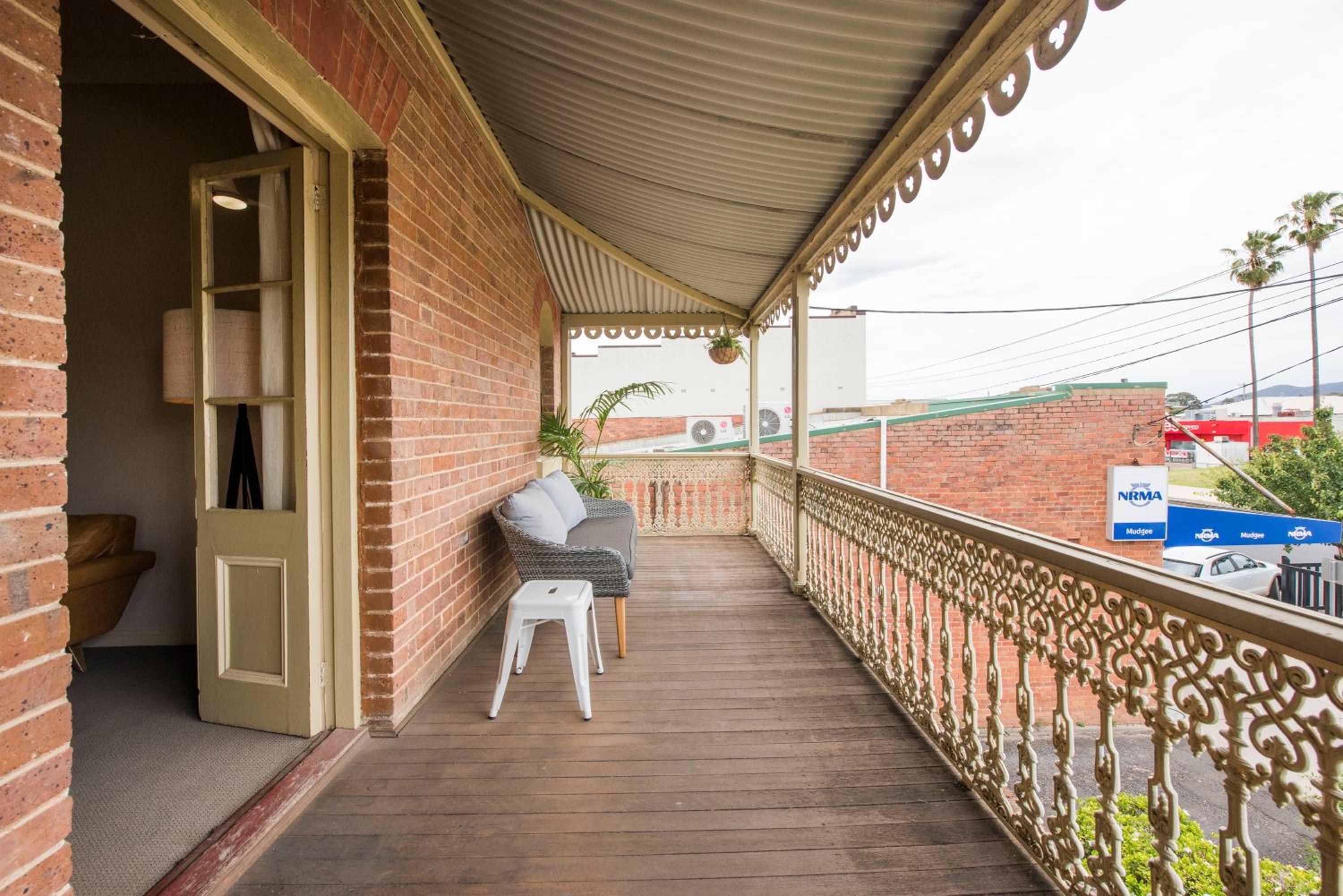A covered balcony with a wooden floor, a white chair, and a small table.