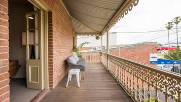 A covered balcony with a wooden floor, a white chair, and a small table.
