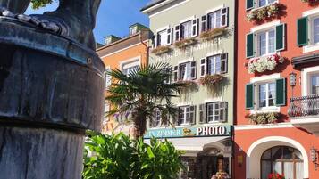Ein Brunnen mit Statue, umgeben von Gebäuden mit Balkonen und Blumenkästen.