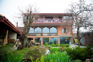 A two-story building with a balcony, surrounded by a garden with various plants and a wheelbarrow. - Savaneti Eco Hotel (Telavi)