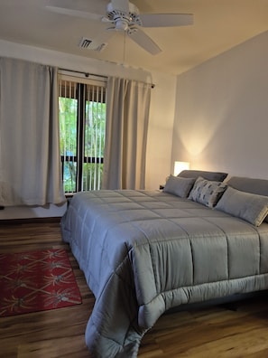 Ein Schlafzimmer mit einem Bett, Vorhängen, einem Deckenventilator und Blick durch ein Fenster.