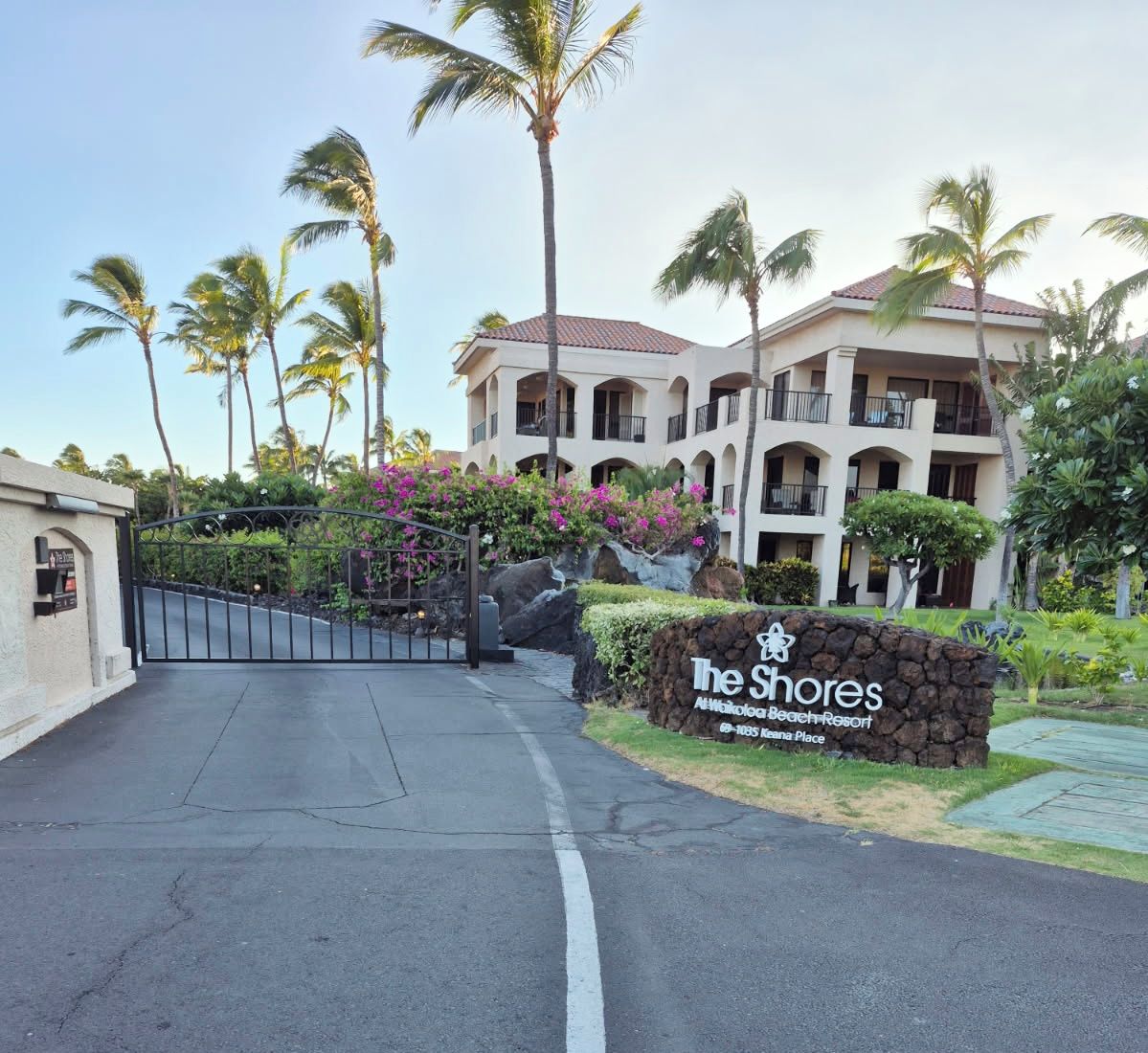 Een omheind toegangshek naar een hotel, met een bord waarop 'The Shores At Waikoloa Beach Resort' staat.