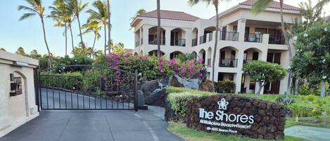 Een omheind toegangshek naar een hotel, met een bord waarop 'The Shores At Waikoloa Beach Resort' staat.