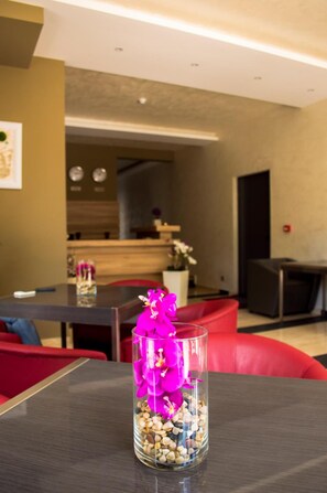 A modern living room with a dining area, a kitchen in the background, and a glass vase with pink flowers on a table. - Hotel Calipso Hotel (Sofia)