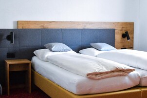 A double bed with white bedding and two pillows, a wooden nightstand, and a headboard with a light switch.