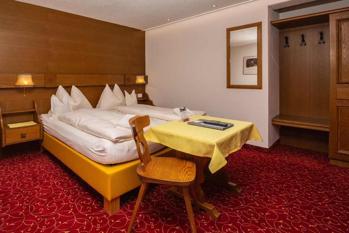 Habitación de hotel con cama, mesita de noche, silla, mesa con mantel amarillo y armario.