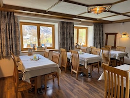 Un comedor con varias mesas y sillas, ventanas amplias con cortinas y techo de madera.
