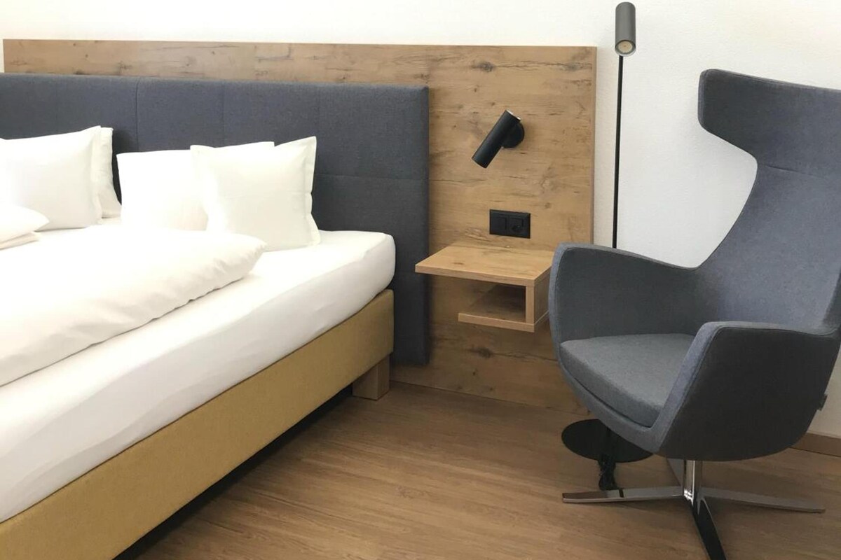 Una habitación de hotel con una cama, una mesita de noche, una silla y una lámpara de pie.