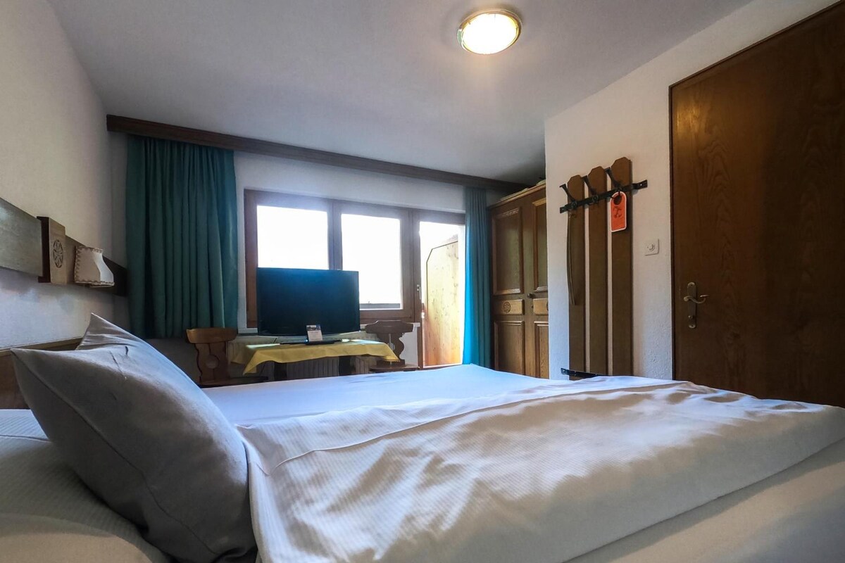 Una habitación de hotel con una cama, televisión, escritorio y armario.