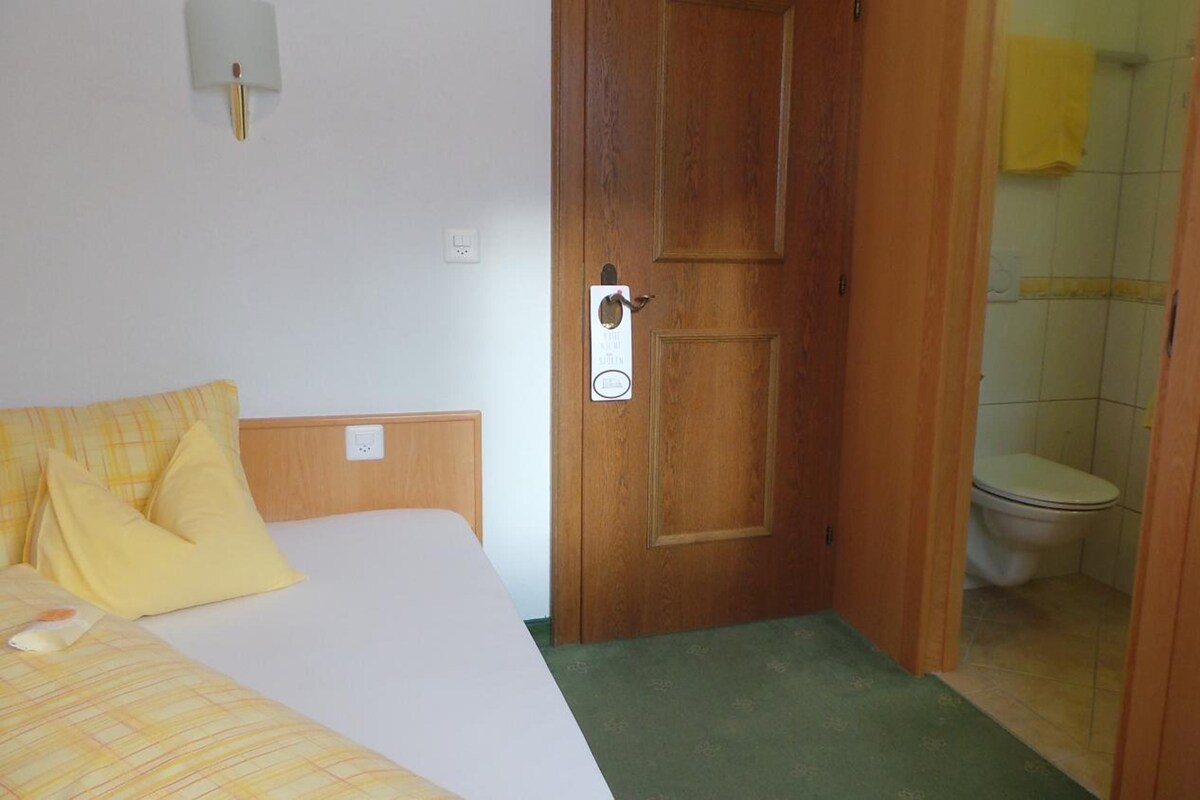 Habitación de hotel con cama, puerta de madera, baño con inodoro y espejo.