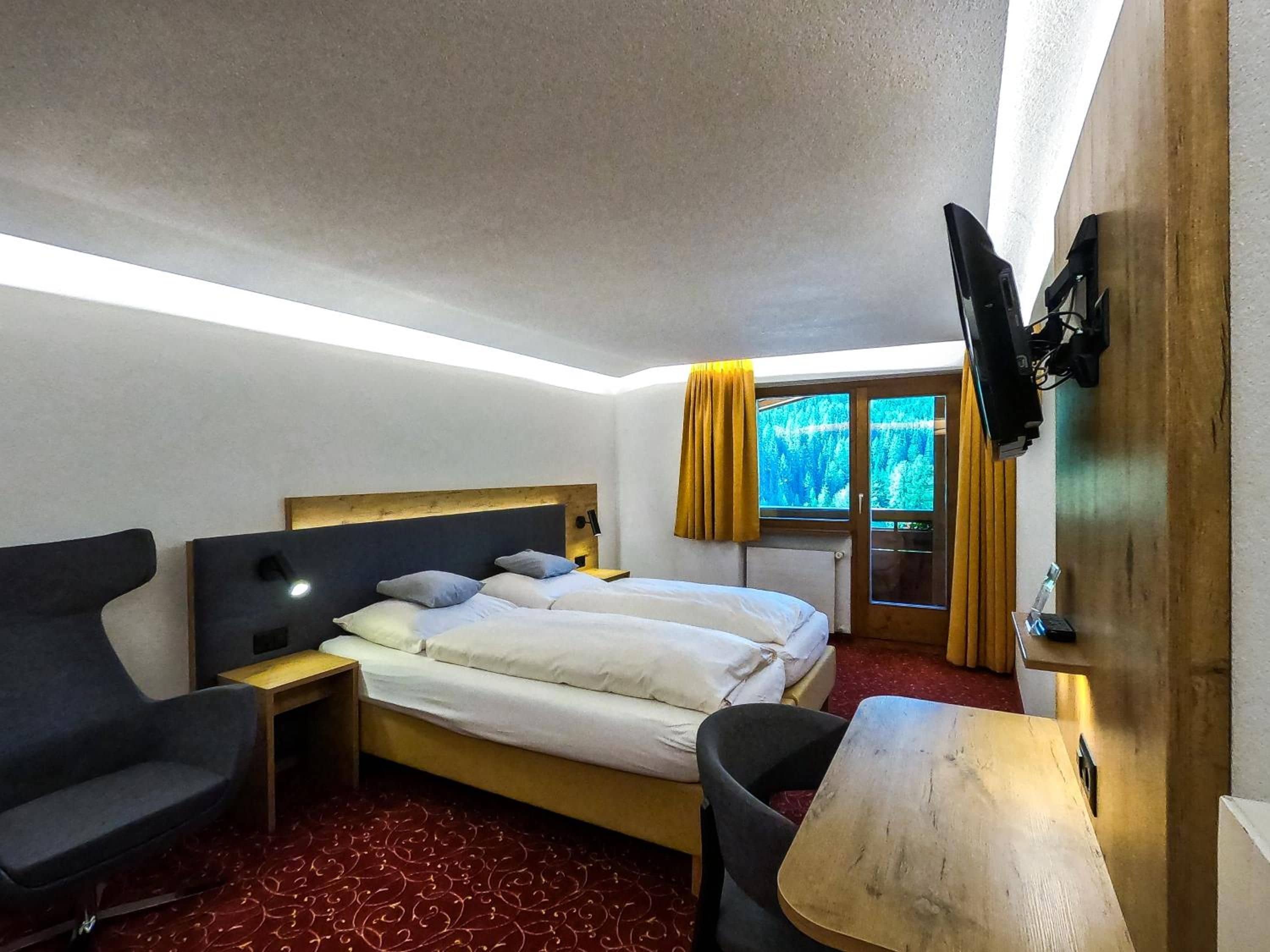 A hotel room with a bed, a desk, a chair, a TV, and a window with curtains.