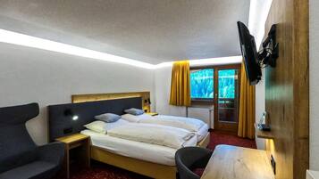 A hotel room with a bed, a desk, a chair, a TV, and a window with curtains.