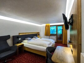 A hotel room with a bed, a desk, a chair, a TV, and a window with curtains.