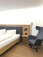 A hotel room with a bed, a nightstand, a chair, and a floor lamp.