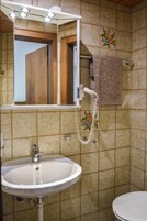 A bathroom with a white sink, a mirror with lights, a towel rack with a towel, and a shower area.