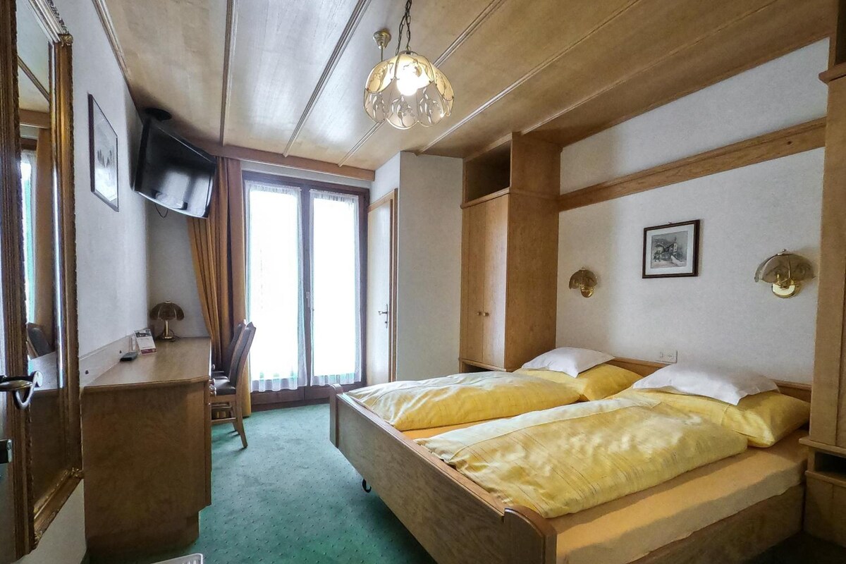 Una habitación con cama, escritorio, silla, televisor y ventana.