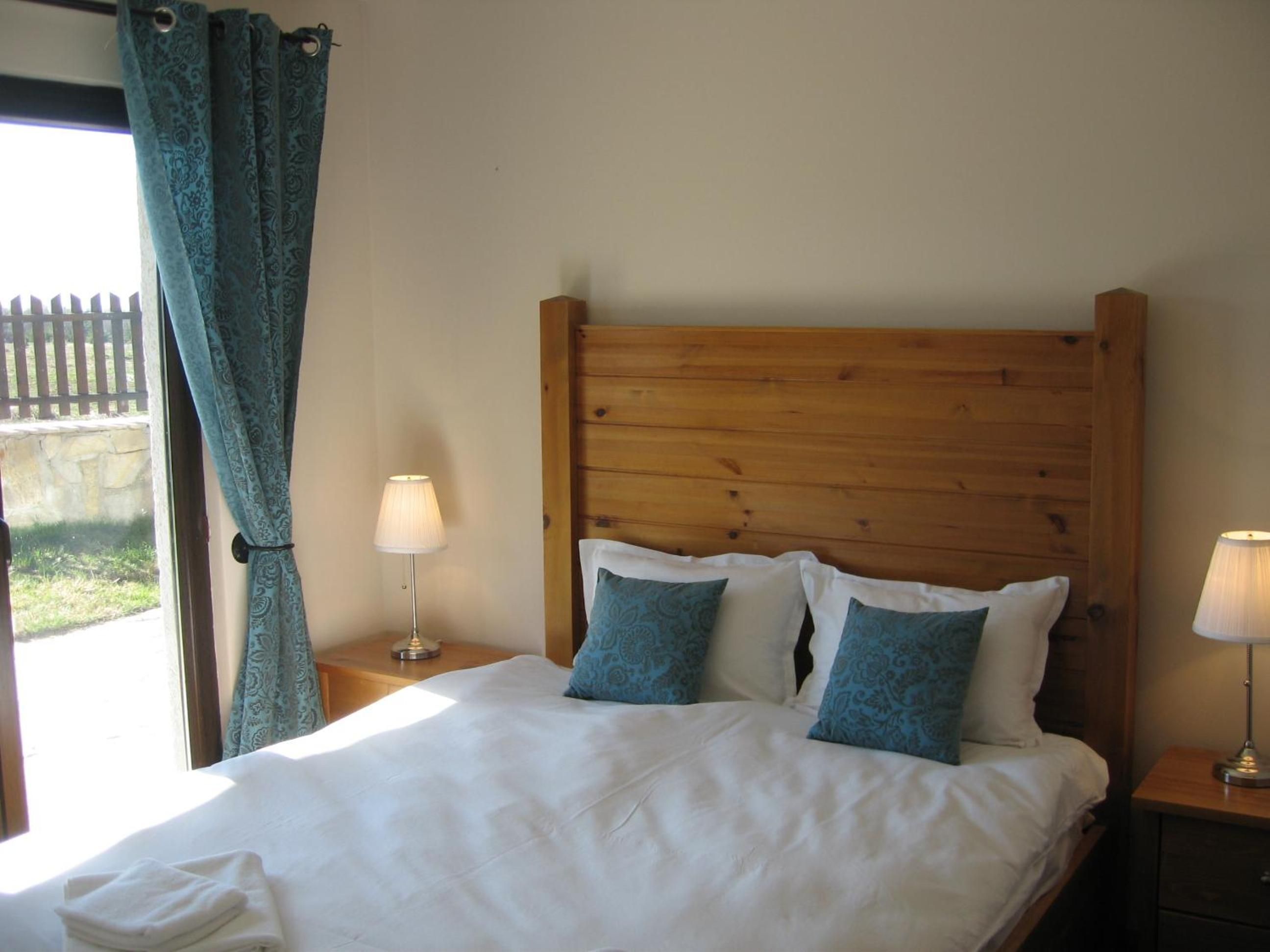 A neatly made bed with white linens and blue patterned pillows, a wooden headboard, and two bedside lamps on wooden nightstands.
