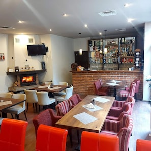 A restaurant with a brick fireplace, multiple dining tables, and a bar area with a variety of bottles. - Chamkoria Chalets (Samokov)