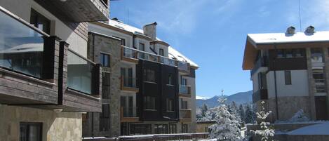 Un edificio moderno de varios pisos con balcones, fachada de piedra y paisaje nevado.