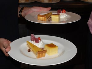 A person holding a plate with a dessert consisting of a slice of pie, a square piece of cheesecake, and a dollop of whipped cream topped with raspberries. - The Bull At Great Totham Limited (Maldon)