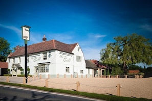 A white building with 'the Bull' written on the facade, a gravel driveway, and a chain-link fence. - The Bull At Great Totham Limited (Maldon)