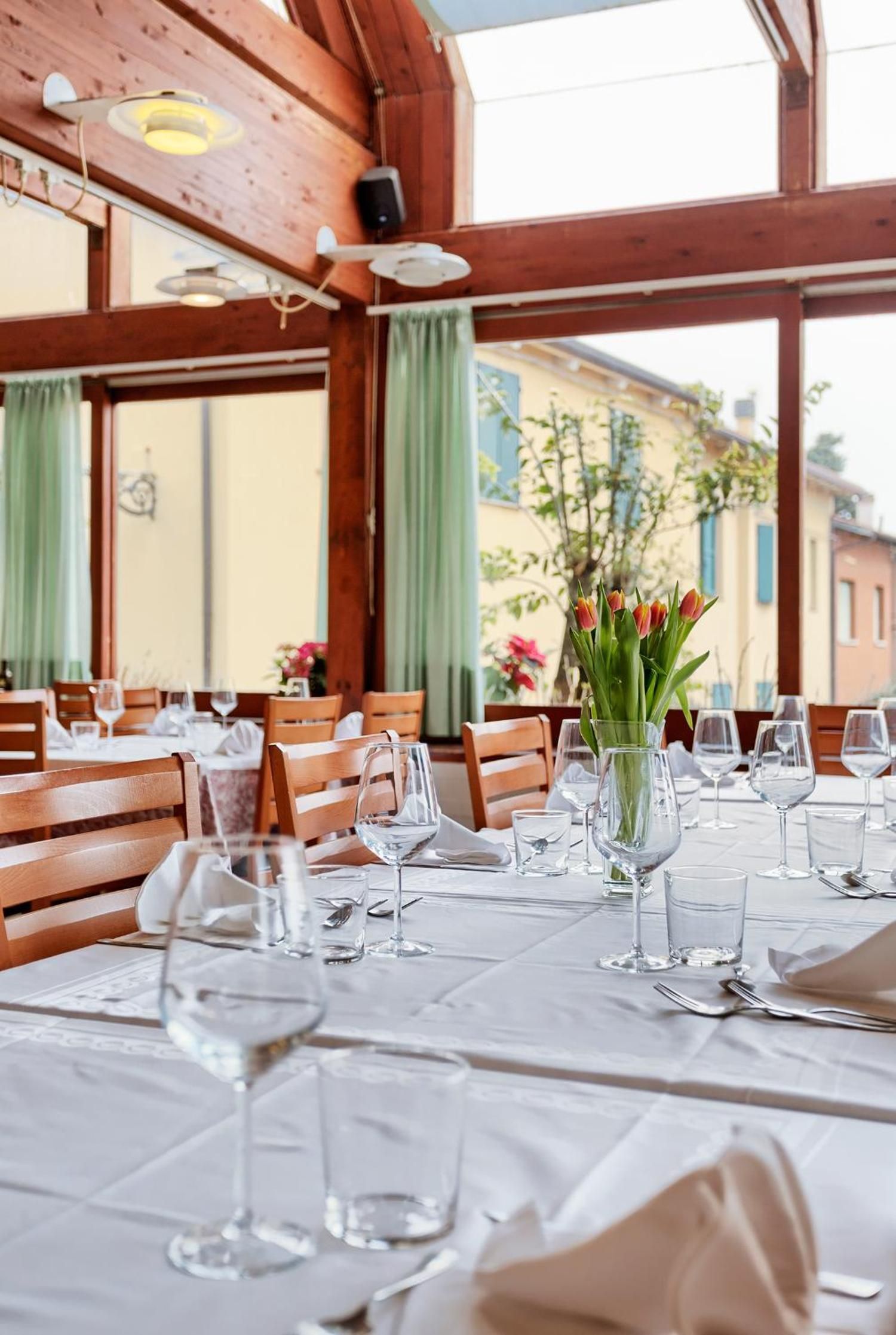A restaurant with wooden beams, large windows, and tables set for dining.