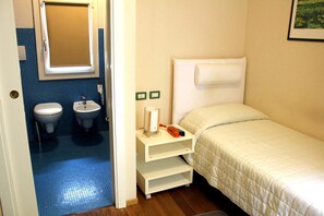 Un alojamiento pequeño y de una sola habitación con cama, mesita de noche con lámpara, inodoro y lavabo.