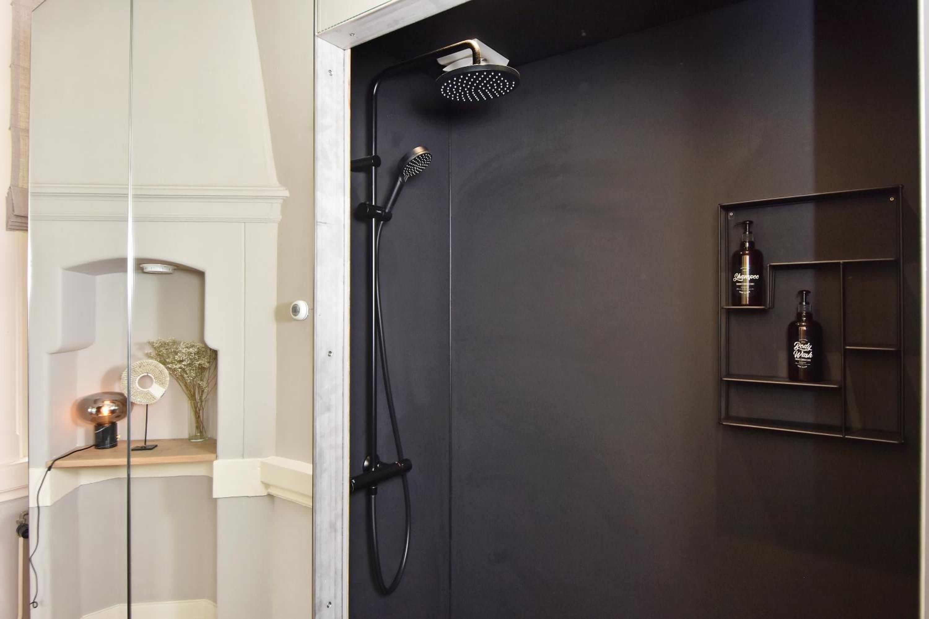 Een moderne badkamer met een douche, een wastafel met spiegel en een plank met toiletartikelen.