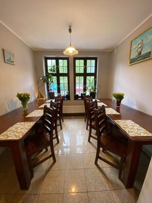 Un comedor con una mesa larga, sillas, plantas en macetas y un cuadro en la pared.