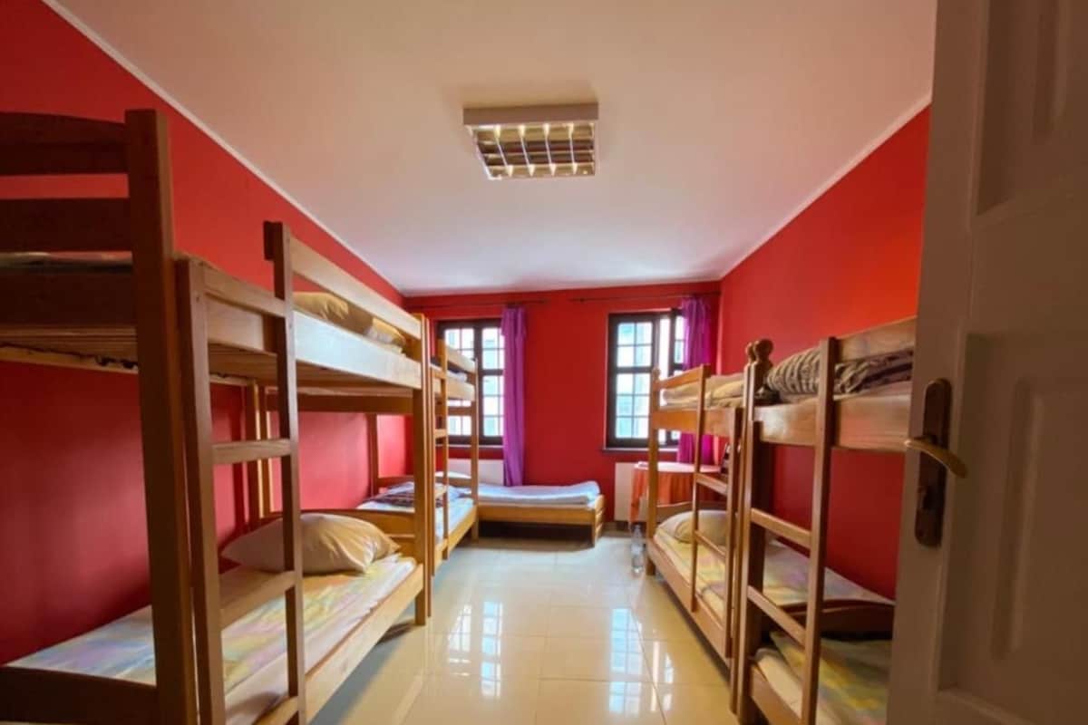 A dormitory room with bunk beds, a tiled floor, and a window with purple curtains.