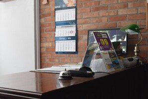 Una mesa de recepción con un calendario, un expositor para folletos, una lámpara de escritorio y un teléfono.