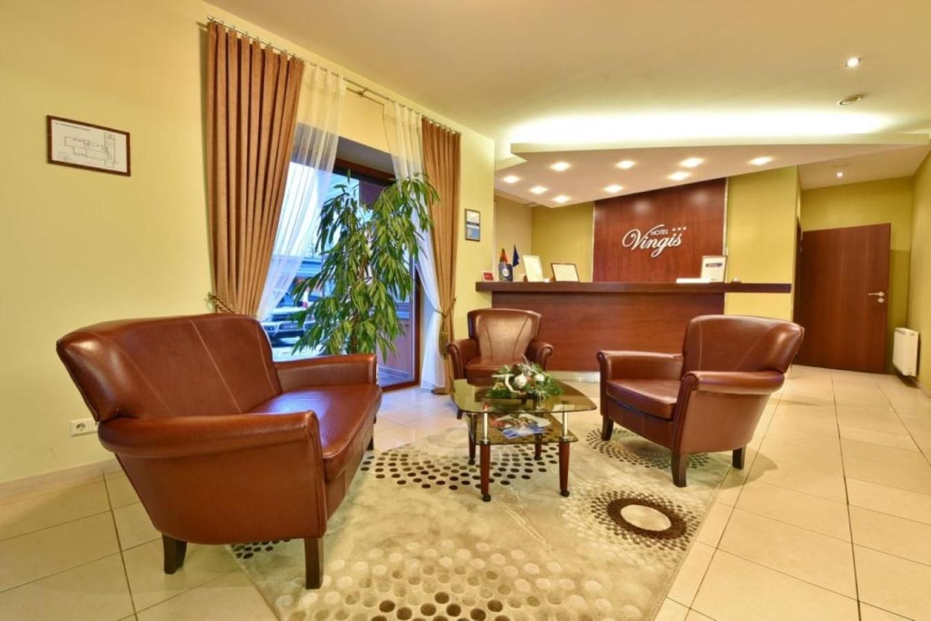 A hotel reception area with leather chairs, a reception desk, and a large window with curtains.