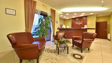 Een hotel receptie met lederen stoelen, een receptiebalie en een groot raam met gordijnen.